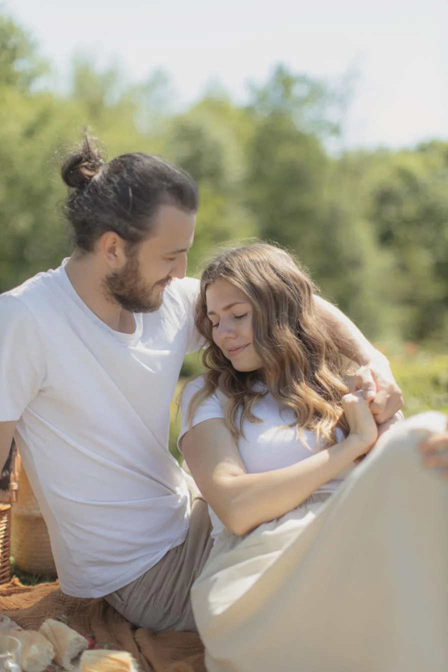 Adam and Lora sitting close together outdoors, foreheads touching, during a quiet afternoon picnic.