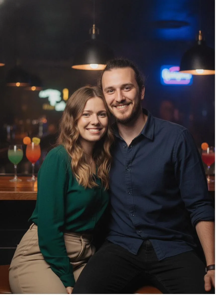 Adam and Lora sitting close together at a bar, smiling, with colourful drinks nearby.